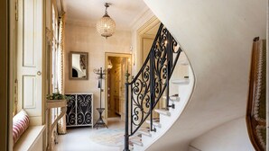 Una imponente escalera con barandillas negras ornamentadas, un candelabro y un espejo en la pared.