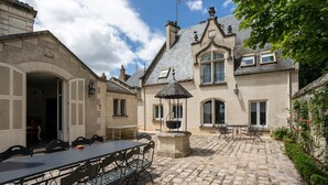 Un patio con una mesa y sillas de piedra, una fuente y un edificio con tejado de azulejos y ventanas de arco.
