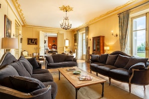 Een ruime woonkamer met twee donkere leren banken, een houten salontafel en een kroonluchter.