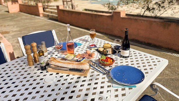 An outdoor dining table with food, drinks, and condiments.