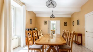 Een eetkamer met een grote houten tafel, meerdere stoelen en een kroonluchter.