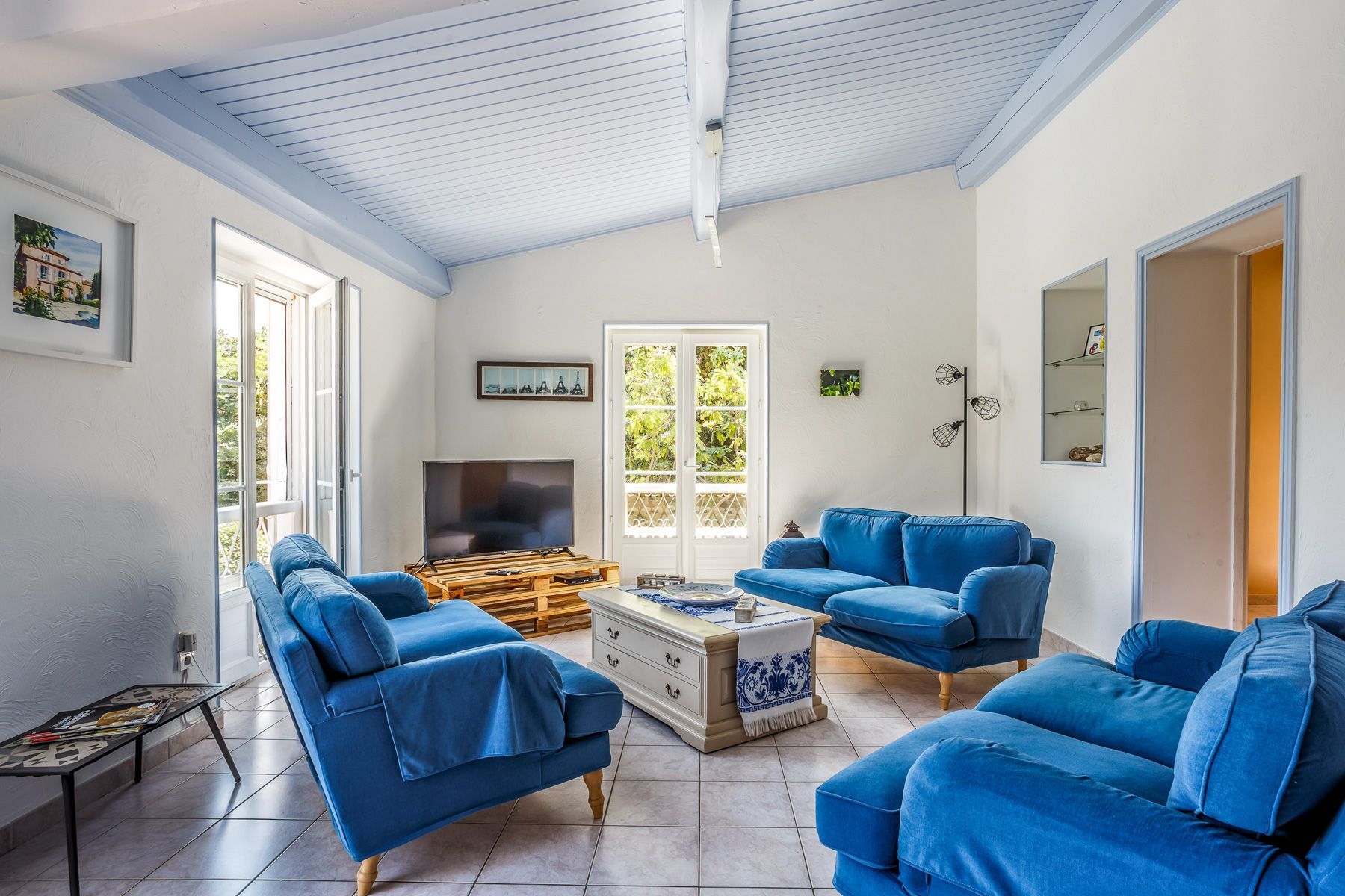 A living room with a TV, two blue sofas, a coffee table, and a large window with a view of greenery.
