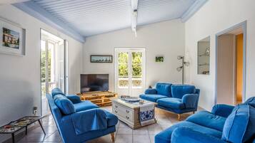 A living room with a TV, two blue sofas, a coffee table, and a large window with a view of greenery.