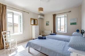 A bedroom with two beds, a chair, a dresser, and a window with curtains.
