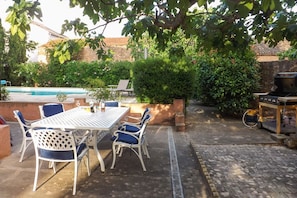 Eine Terrassenausstattung mit Tisch, Stühlen, Grill und Schwimmbecken im Hintergrund.