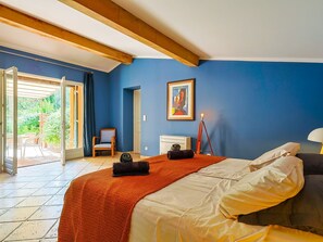 Een slaapkamer met een bed, een stoel, een bureau, een lamp en een schilderij aan de muur.