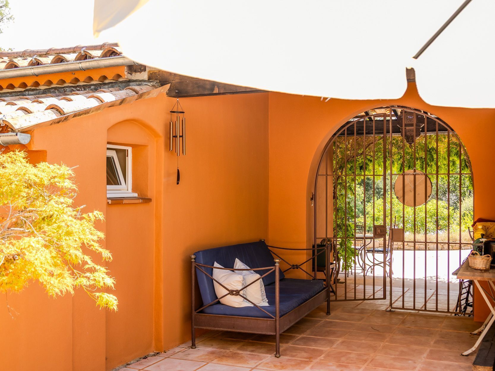 A cozy outdoor seating area with a blue cushioned bench, a metal gate, and a tiled floor.