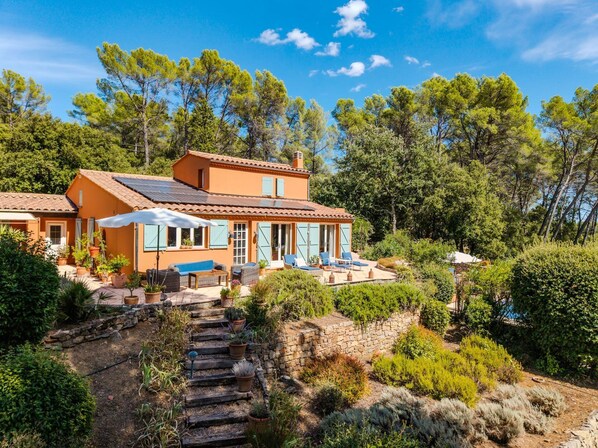 Een villa in mediterrane stijl met een stenen trap die leidt naar een terras, omringd door weelderige begroeiing en bomen.