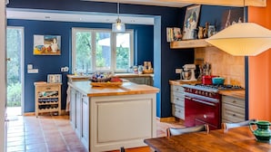 Una cocina con una isla central, una estufa roja y una zona de comedor con mesa y sillas.
