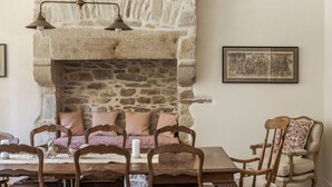 Une salle à manger rustique avec une cheminée en pierre, des chaises en bois et une table dressée pour deux personnes.