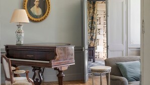 Un piano, une chaise, une table et un canapé dans une pièce avec une porte donnant sur un mur de pierre et un rideau à motifs.