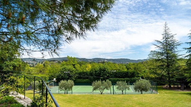 Un court de tennis entouré d’arbres, avec une vue sur la montagne.