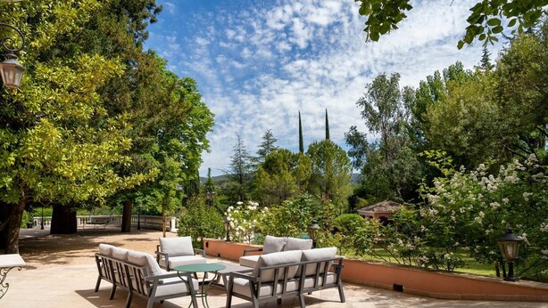 An outdoor patio with seating and tables, surrounded by lush greenery and trees.
