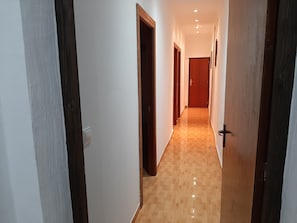 A hallway with wooden doors and a tiled floor, leading to a room with a wooden door.