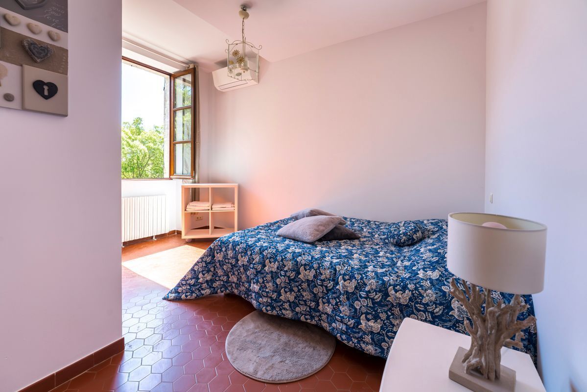 Um quarto com cama, tapete redondo, mesa de cabeceira, luminária, janela e radiador.