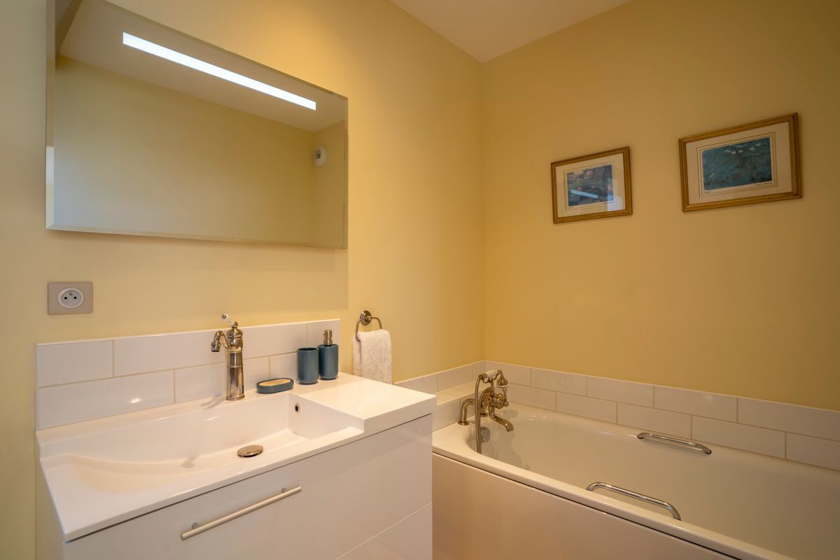 Un baño con un lavamanos blanco, una bañera y dos cuadros en la pared.