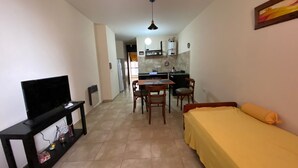 A compact living space with a TV, a bed, a dining table with chairs, and a kitchen area in the background. - Downtown Apartment (VILLA MARIA)