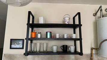 A kitchen with a black shelf unit holding various kitchenware and a framed picture on the wall.
