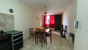 A compact kitchen with a stove, dining table, and chairs. A red curtain and a hanging light fixture are visible. - Downtown Apartment (VILLA MARIA)