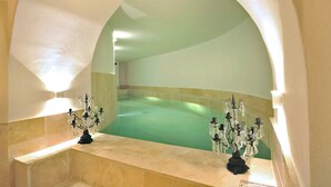 Un área de spa con una bañera grande y curvada bajo un arco semicircular, flanqueada por dos candelabros decorados.