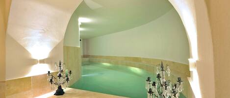A spa area with a large, curved bathtub under a semi-circular archway, flanked by two ornate chandeliers.
