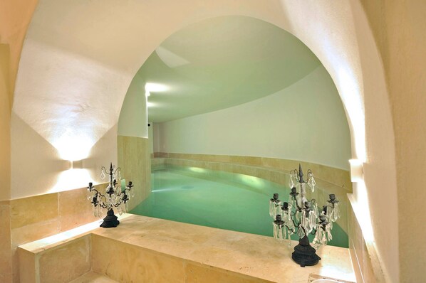 A spa area with a large, curved bathtub under a semi-circular archway, flanked by two ornate chandeliers.