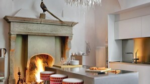 Una cocina moderna con una isla central, taburetes de bar, chimenea y una araña.