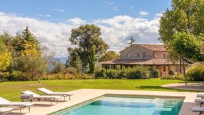 Una piscina con sillas de descanso, un edificio de piedra y follaje circundante.