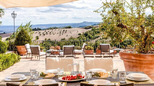 Un área de comedor al aire libre con mesas dispuestas para una comida, con vistas a un paisaje pintoresco.