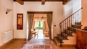 A hallway with a wooden ceiling, a staircase, a radiator, a patterned rug, and a dining area with a table and chairs.