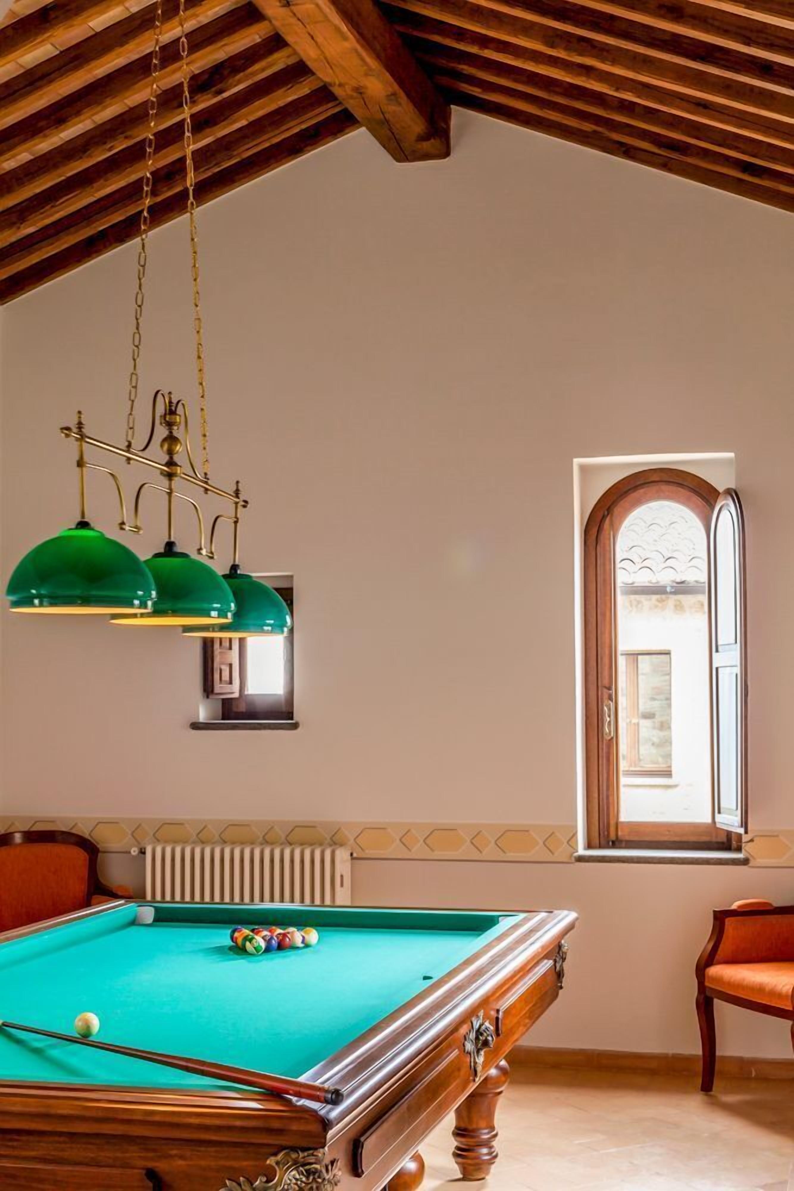 Una mesa de billar en una sala con techo de madera y un ventanal de diseño arqueado.