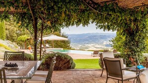 An outdoor patio with a table, chairs, and a view of a pool and mountains.