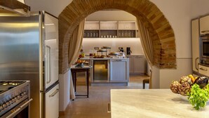 A modern kitchen with an arched brick feature, stainless steel appliances, and a central island with a bowl of vegetables.