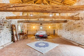 Una habitación rústica de paredes de piedra y techo de madera, con una cama, una silla, una mesa y una alfombra.