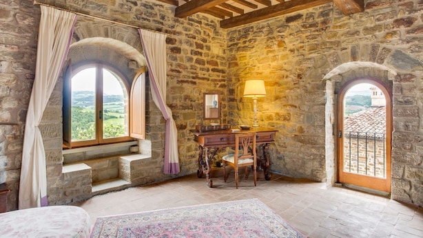 A rustic stone room with a wooden desk, a chair, and a lamp. There are two windows with curtains, one of which has a view of greenery outside. - Castello Gubbio - Fifteen Bedroom Castle, Sleeps 30 (Gubbio)