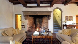 A cozy living room with a fireplace, two sofas, a coffee table with wine glasses and snacks, and a staircase in the background. - Casa Poggio - Four Bedroom Villa, Sleeps 12 (Cassia)