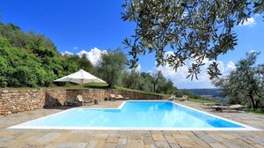 A rectangular swimming pool with a stone border, surrounded by a stone wall and a stone patio. There are lounge chairs and a white umbrella providing shade. - Casa Poggio - Four Bedroom Villa, Sleeps 12 (Cassia)