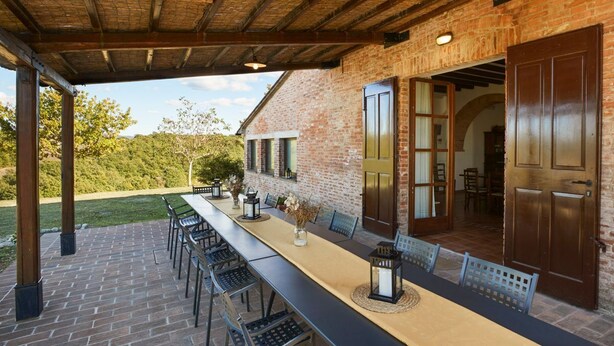 Eine Terrassenausstattung mit langem Tisch und Stühlen, einer Ziegelwand und einer Holzbeschichtung.