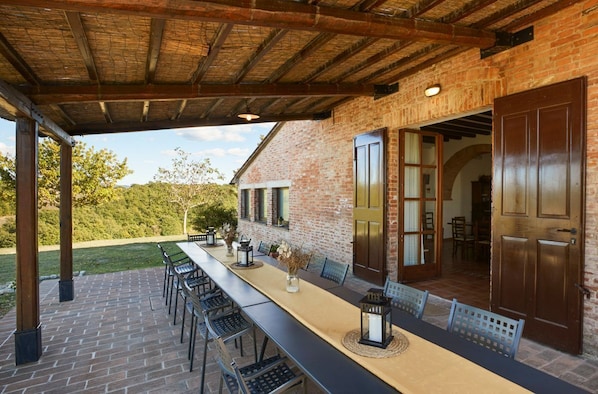 Une terrasse extérieure avec une longue table et des chaises, un mur en briques et un plafond en bois.