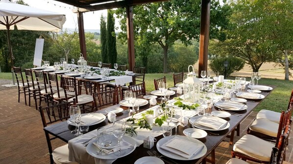 Un espace de restauration en plein air avec plusieurs tables dressées pour un repas, entourées de chaises et agrémentées de plantes.