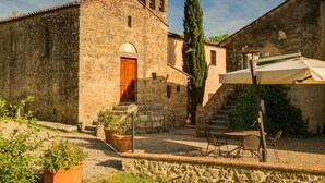 A stone building with a wooden door and a bell tower, a staircase, and outdoor seating with a table and chairs.