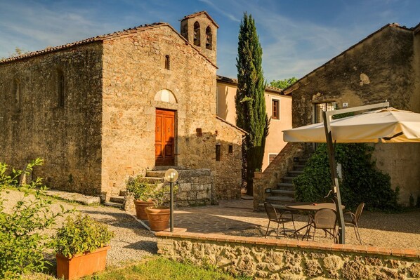 A stone building with a wooden door and a bell tower, a staircase, and outdoor seating with a table and chairs.
