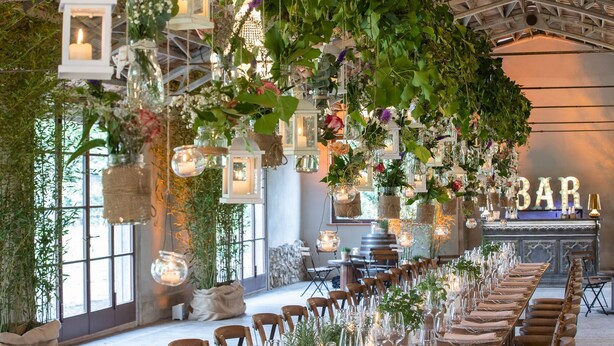 A long banquet table set for a formal event, with hanging lanterns and greenery.