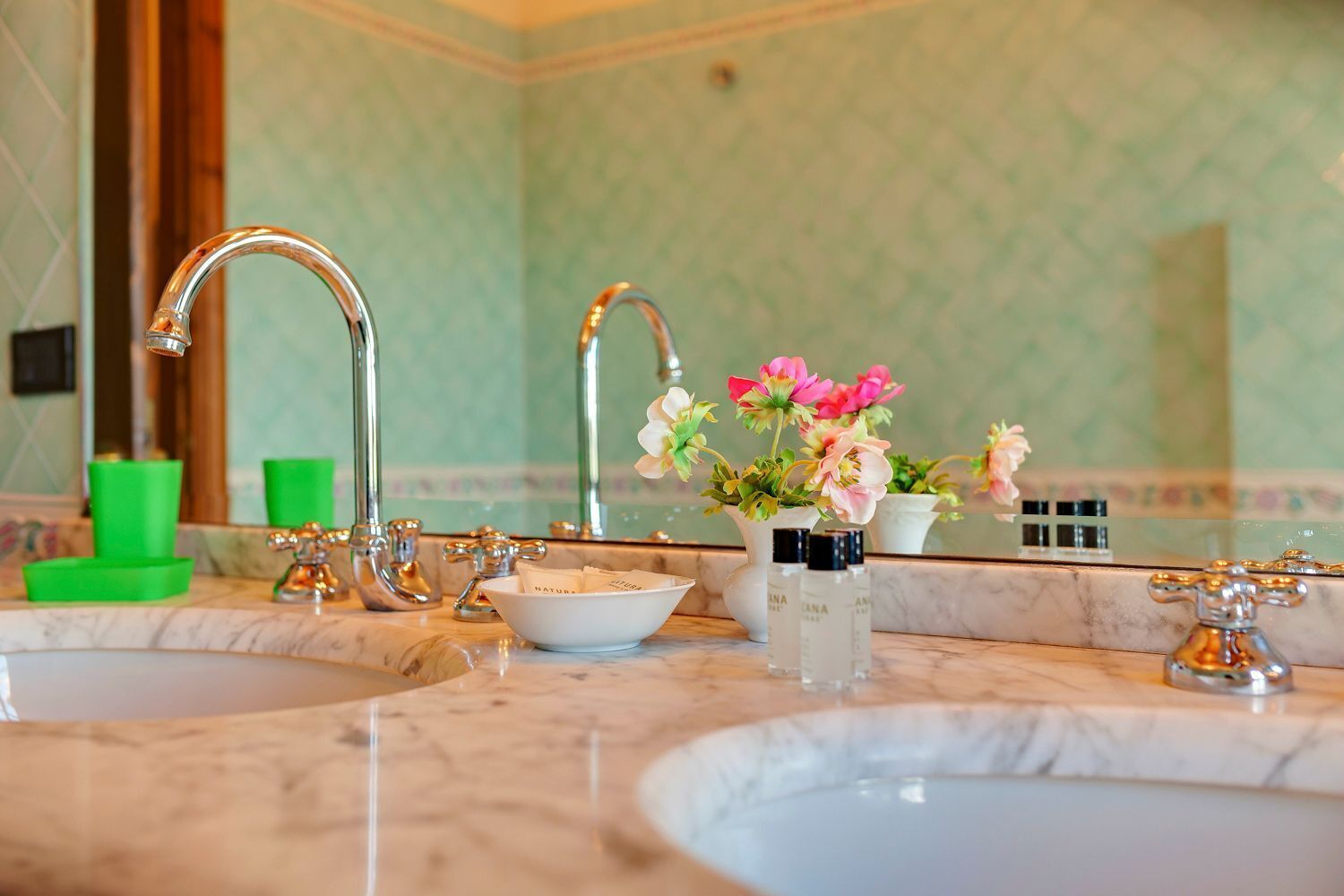 Une salle de bain avec deux lavabos, un miroir et un vase rempli de fleurs.