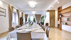 Un comedor con una mesa larga dispuesta para una comida, rodeada de sillas, con una chimenea y estanterías al fondo.