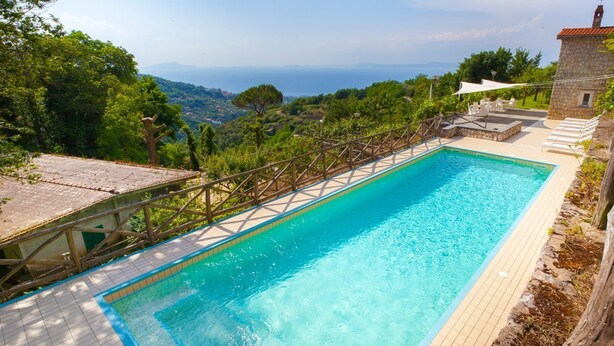 Una piscina rectangular con un deck de madera y una pared de piedra en un lado.