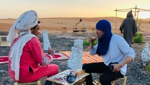 Two people sitting on a mat outdoors with a table between them.