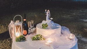 Un pastel de bodas con un adorno, una botella de champán, copas y un farol sobre una mesa.