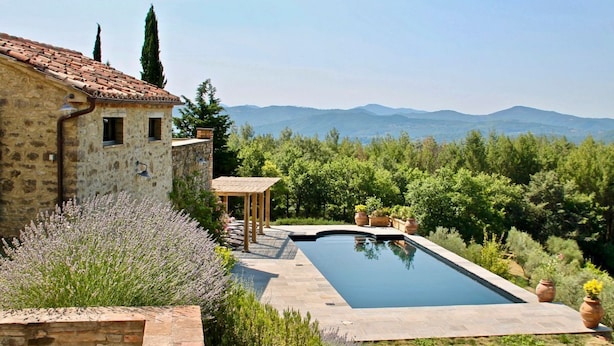 Un bâtiment en pierre avec un toit en tuiles, une piscine et une vue sur les montagnes.