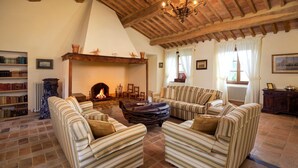A cozy living room with striped sofas, a fireplace, a bookshelf, and a rustic ceiling.